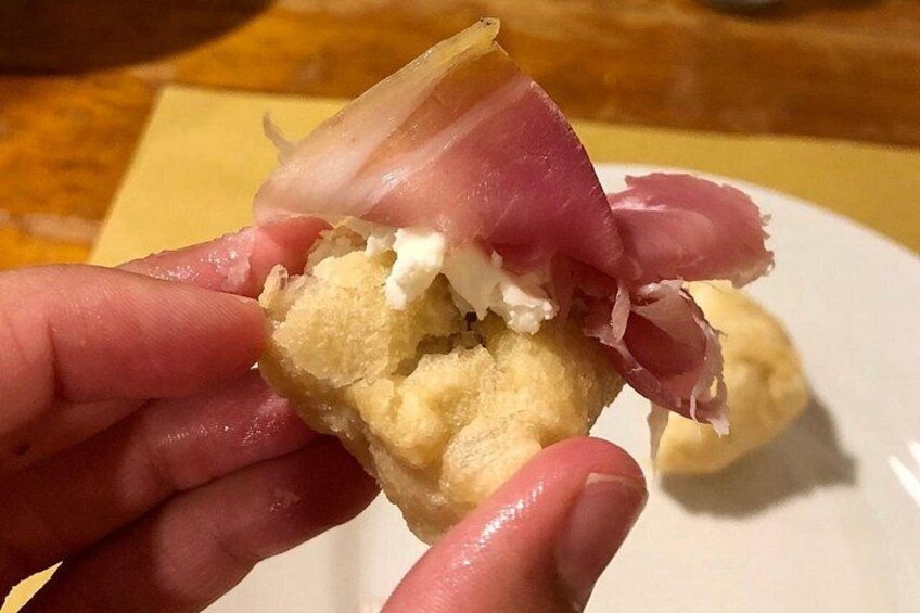 A hand holding a biscuit with a piece of meat and a dollop of cream. 5