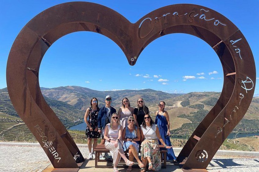 A heart-shaped monument with inscriptions, a group of people posing in front of it, and a mountainous landscape in the background. 1