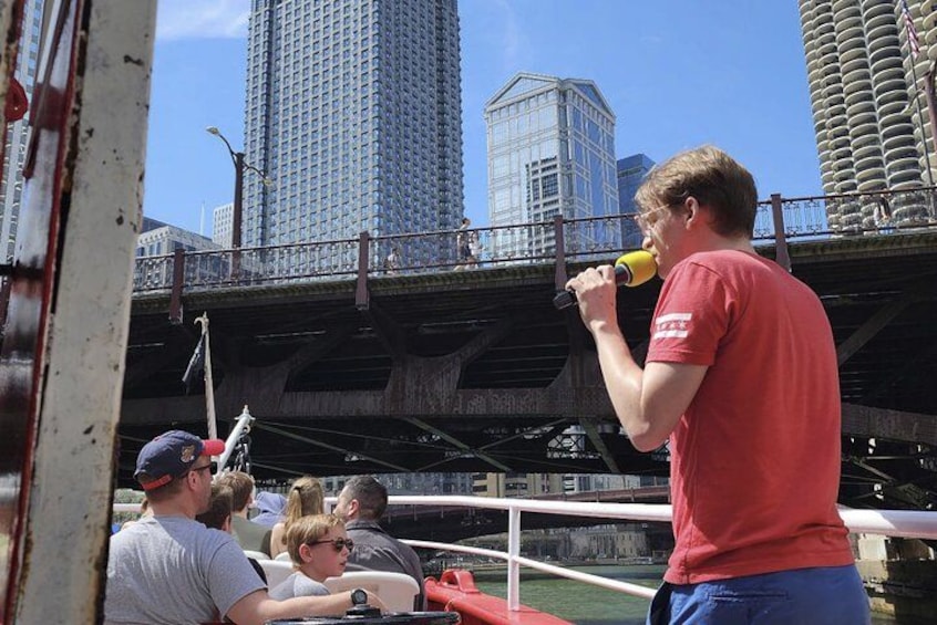 Una persona hablando en un micrófono, un puente y edificios altos al fondo. 2