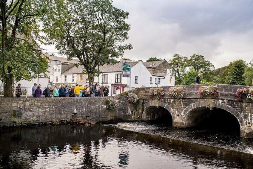 A stone bridge over a river with people gathered on it, surrounded by buildings and trees. 4