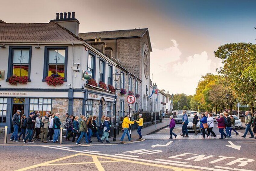 A busy street with pedestrians crossing, a pub with outdoor seating, and a clock tower. 3