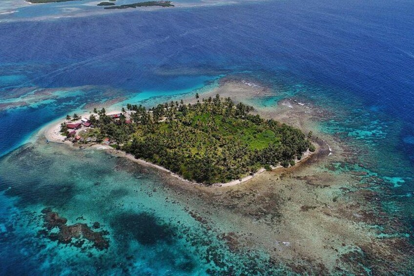 An aerial view of a small island with a dense forest, clear blue waters, and a few buildings. 4