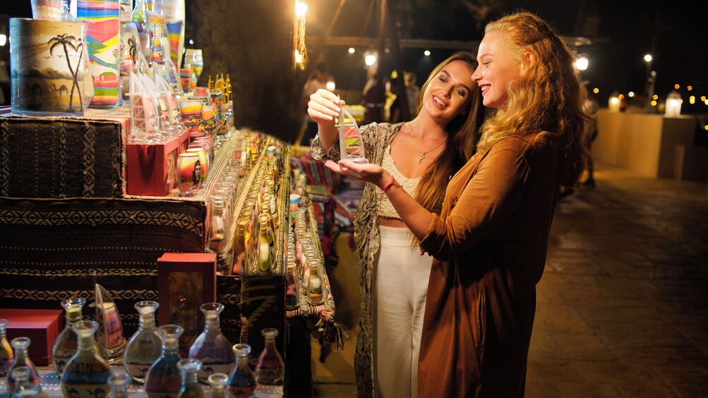 Dos personas observan una exhibición de botellas de vidrio de colores en un mercado. 1