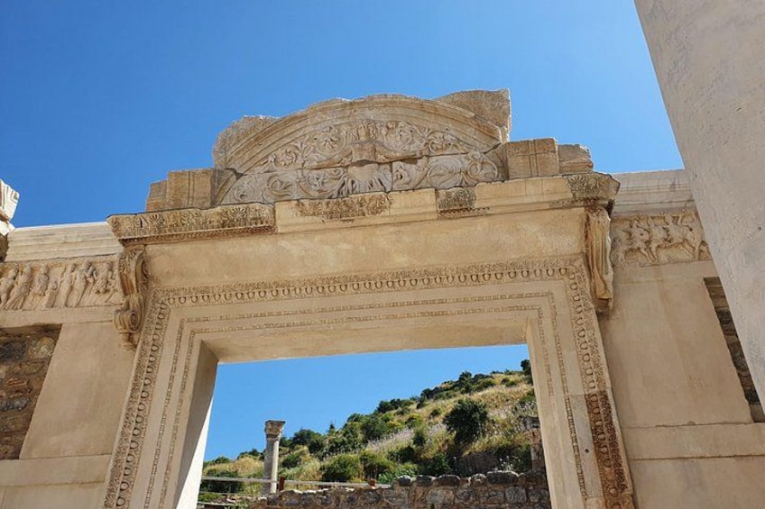 An ancient stone archway with intricate carvings and a view of a hilly landscape in the background. 2
