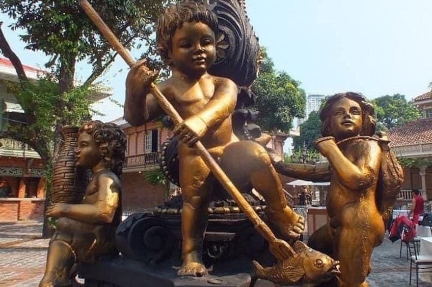 A bronze statue of a seated figure with a child on its lap, a standing child, and a fish. 5