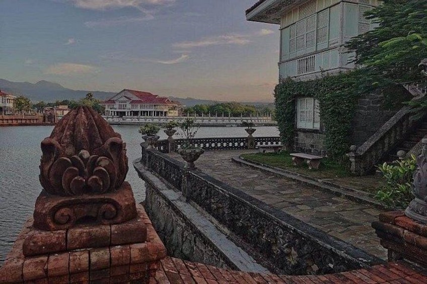 A stone balustrade with a decorative element, a building with a red roof, and a body of water in the background. 3