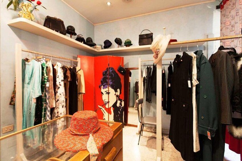 Un magasin de vêtements avec des portants remplis de vêtements, un mannequin et des étagères où sont exposés des chapeaux. 4