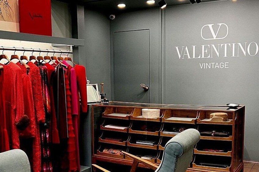 Intérieur d’un magasin Valentino Vintage, avec des vêtements rouges exposés sur des portants, des présentoirs en bois et une porte grise. 3