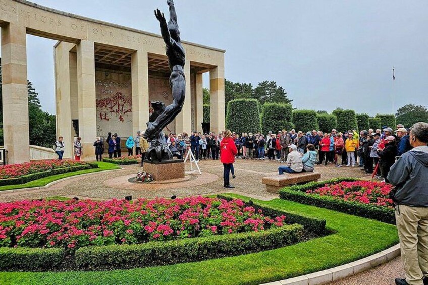 A memorial with a statue, surrounded by flower beds and a crowd of people. 2