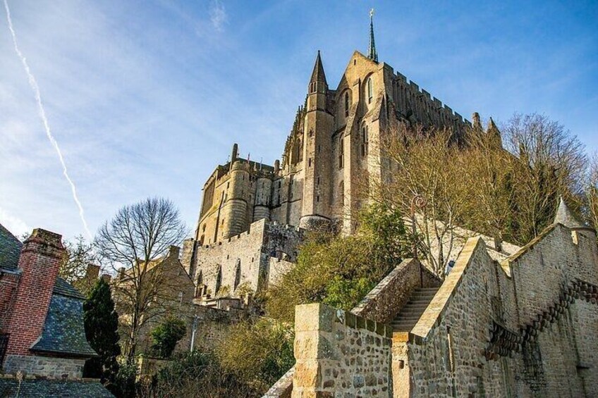 A historic castle with a prominent tower, a stone staircase leading up to it, and a clear blue sky. 3