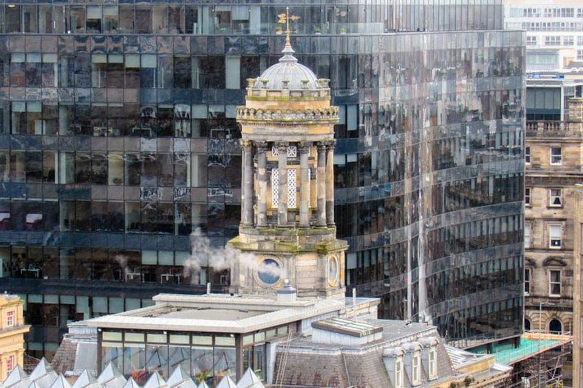 A historic clock tower with a dome, surrounded by modern glass buildings. 2