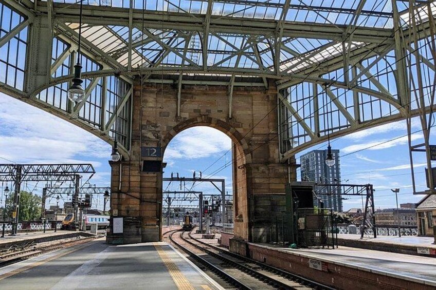 A train station with a large arched bridge, tracks, and a platform. 3