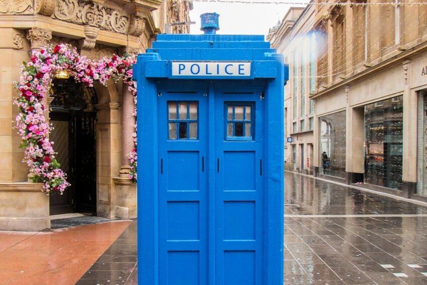 A blue police box with 'POLICE' written on it, located on a wet street with buildings in the background. 5