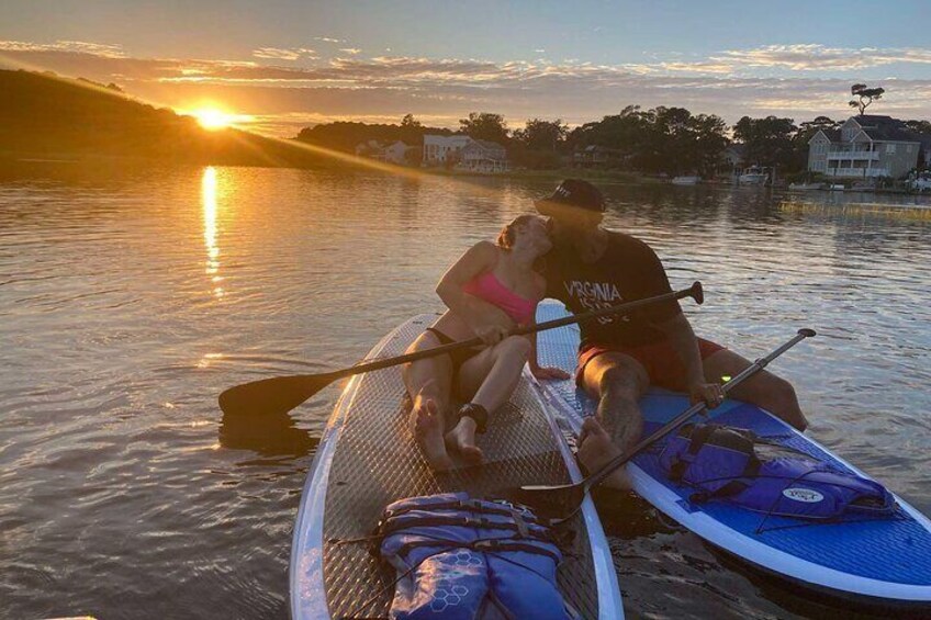 Two people on a paddleboard in calm water during sunset. 1