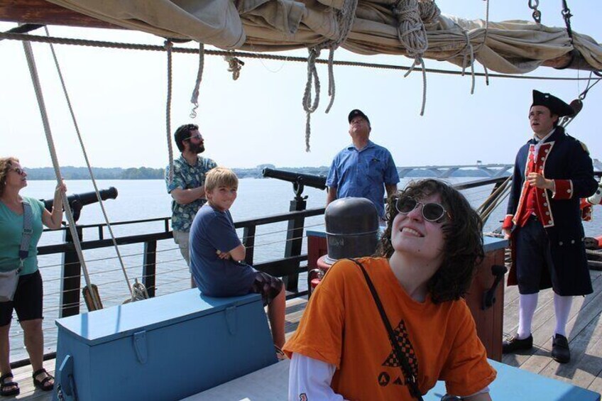 A group of people on a boat with a person in an orange shirt sitting at a table. 4