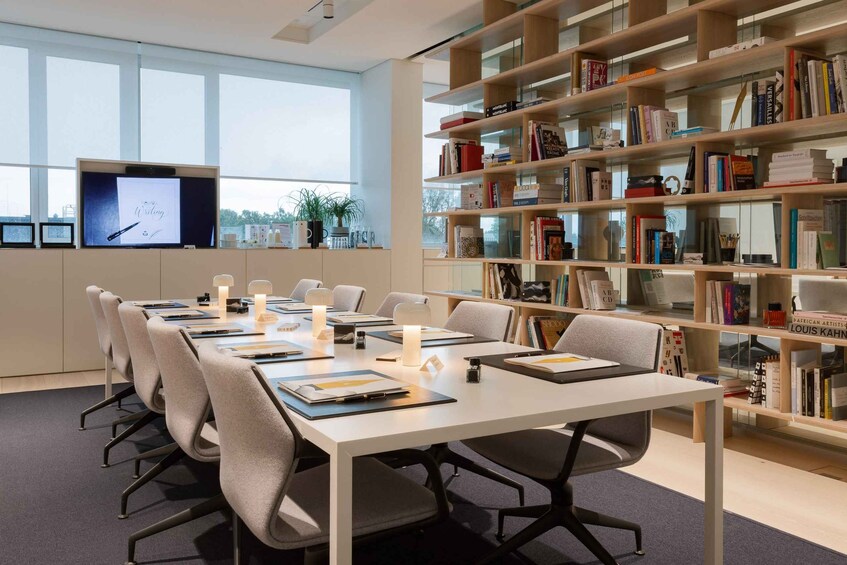 A modern meeting room with a long table, chairs, and a bookshelf filled with books. 5