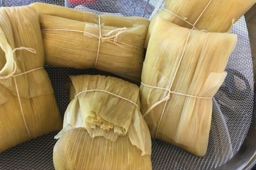 Several tamales wrapped in corn husks tied with string, placed in a mesh basket. 3