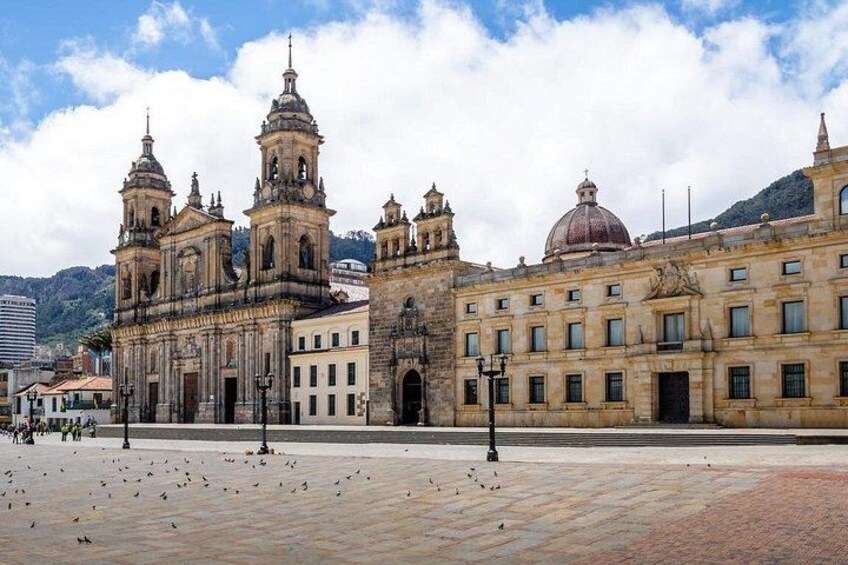 Una cattedrale storica con numerose cupole e campanili, una piazza lastricata e montagne sullo sfondo. 2