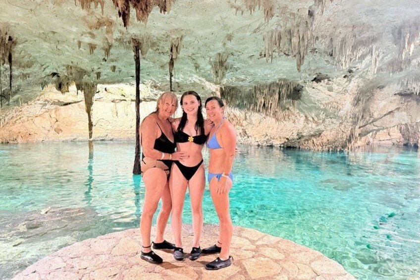 A group of people standing by a clear pool with a cave-like background. 1
