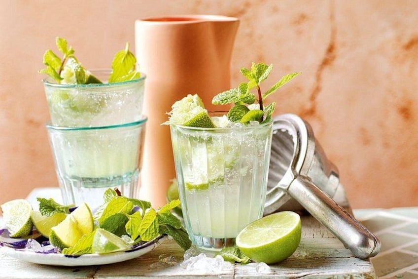 Two glasses of a clear beverage with mint leaves, a lime half, and a metal grater on a wooden surface. 4