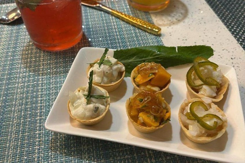 A plate of appetizers with various fillings, a glass of red beverage, and a mint leaf on a textured tablecloth. 3