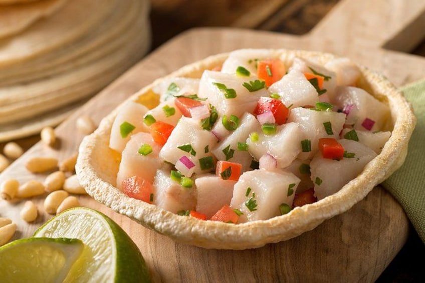 A seafood dish in a bowl, garnished with herbs, with a lime half and pine nuts nearby. 5