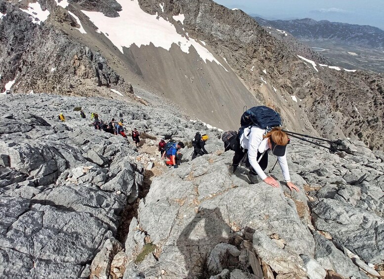 A group of hikers climbing a rocky mountain path with patches of snow. 4