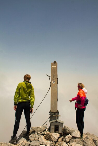 Two people standing on a rocky peak with a tall monument in the center. 1