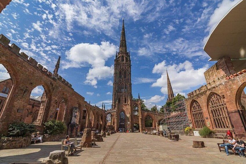 A historic church with a tall spire, arches, and a paved square with benches. 3