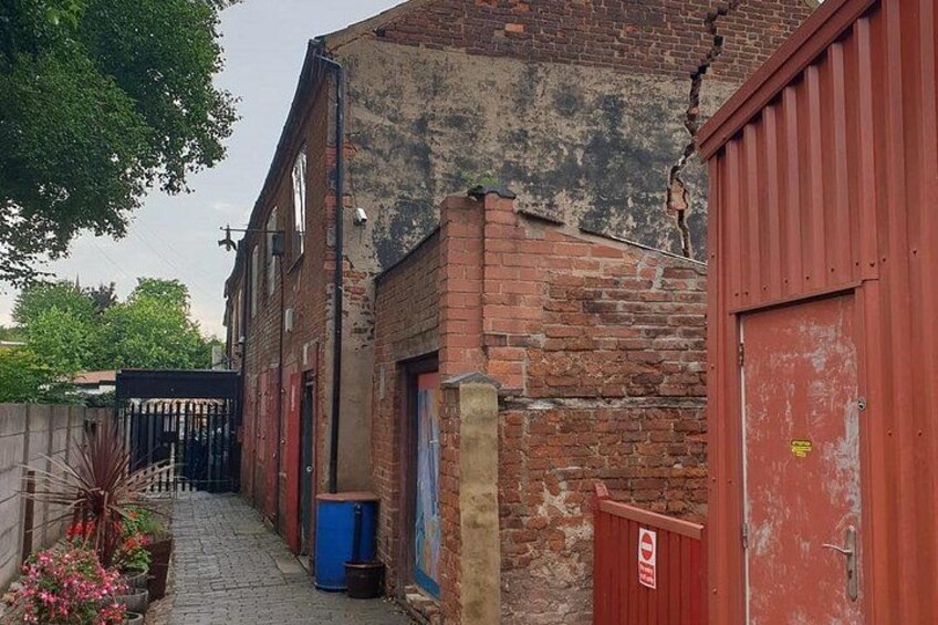 A narrow alleyway with brick buildings, a red gate, and a blue trash bin. 4
