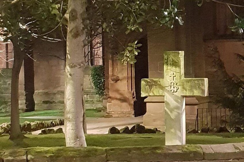 A cemetery with a stone cross and a building in the background. 2
