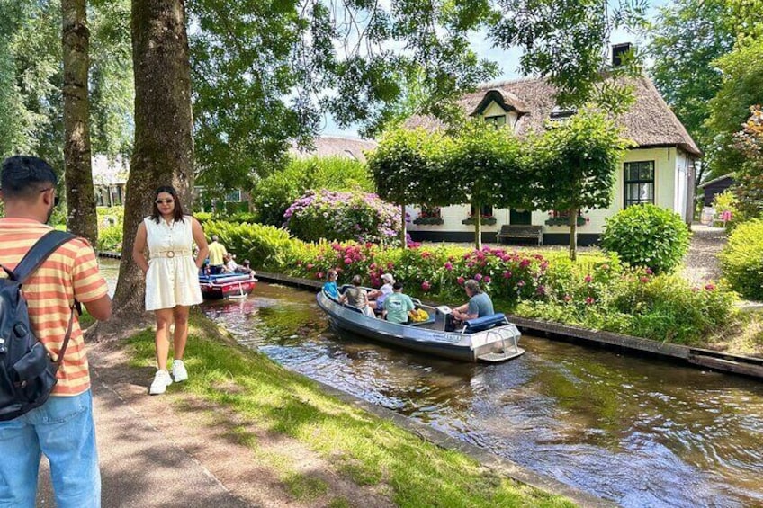 A canal with boats, a woman in a white dress, and a house with a thatched roof. 1