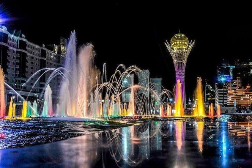 A nighttime cityscape with a brightly lit fountain display and a distinctive tower. 2