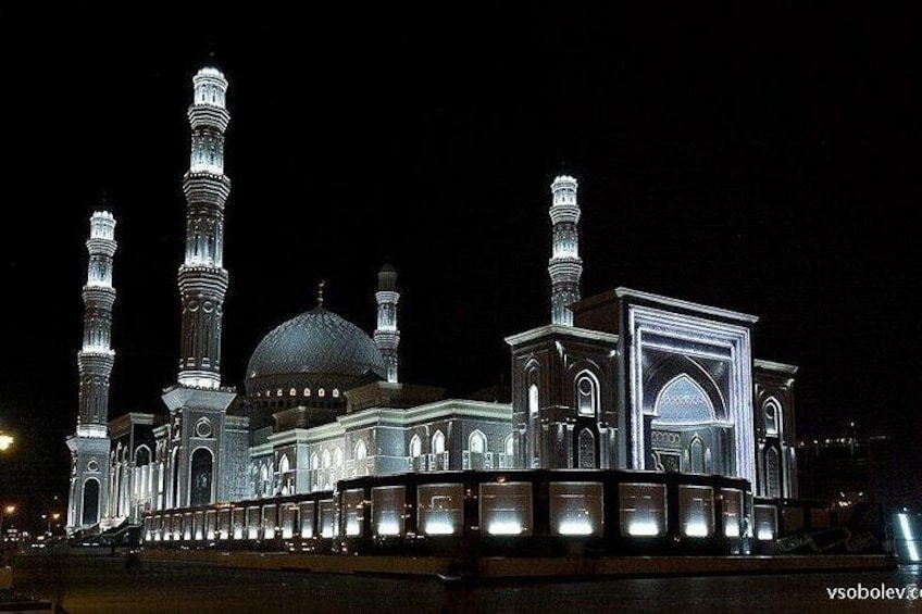 Una mezquita con múltiples minaretes y una cúpula grande, iluminada durante la noche. 1