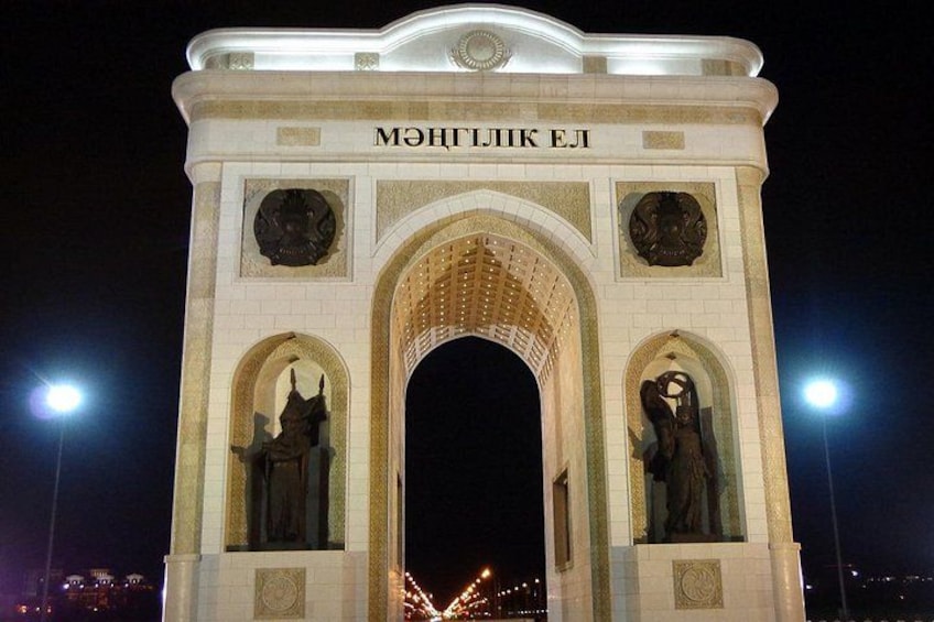 Un gran arco de piedra con inscripciones y estatuas, iluminado por la noche. 5
