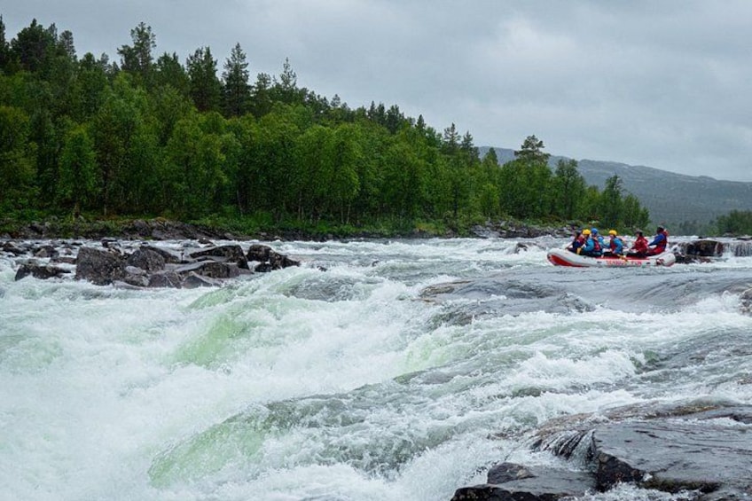 A white water rafting trip with a group of people in a red raft navigating through a river surrounded by dense forest and rocky terrain. 3