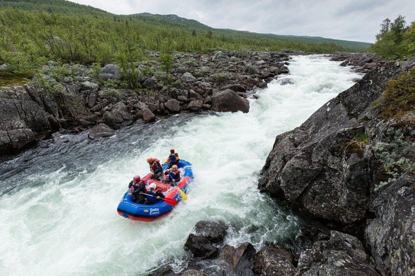 A group of people rafting down a river surrounded by rocky terrain and green hills. 2