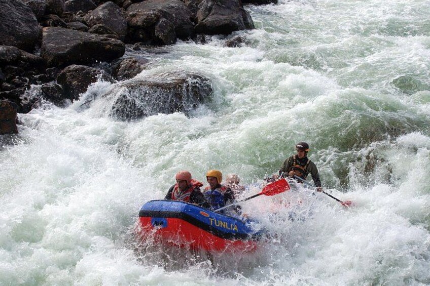 Un viaje de rafting en aguas bravas con una balsa inflable azul y roja que se desplaza entre rápidos turbulentos. 5