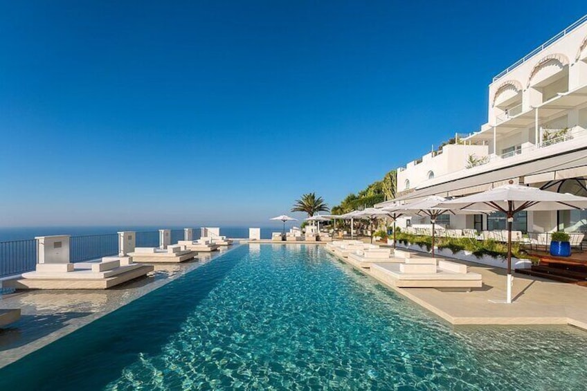 Zona junto a la piscina con sillones reclinables y sombrillas, con vista a un mar azul cristalino. 1