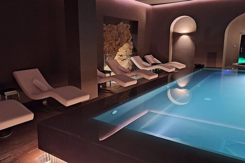 Piscina interior moderna con sillones de descanso y una pared de piedra. 2