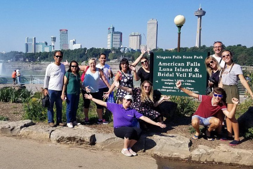 En grupp människor i Niagarafallen statspark, med en skylt som visar parkens läge och dess olika sevärdheter. 1