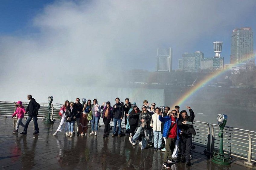 En grupp människor som står på en våt yta med en stadsbild och en regnbåge i bakgrunden. 3