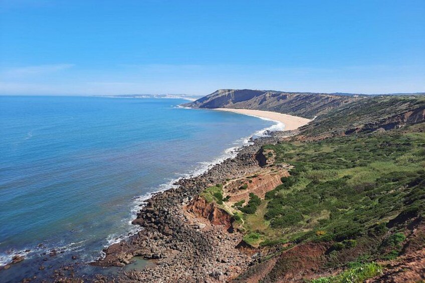 A coastal landscape with a beach, rocky shoreline, and green hills. 1