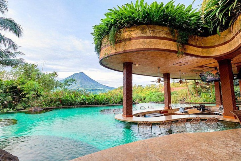 Ein Pool in tropischer Umgebung, im Hintergrund ein Berg und ein überdachter Sitzbereich mit Pflanzen. 5