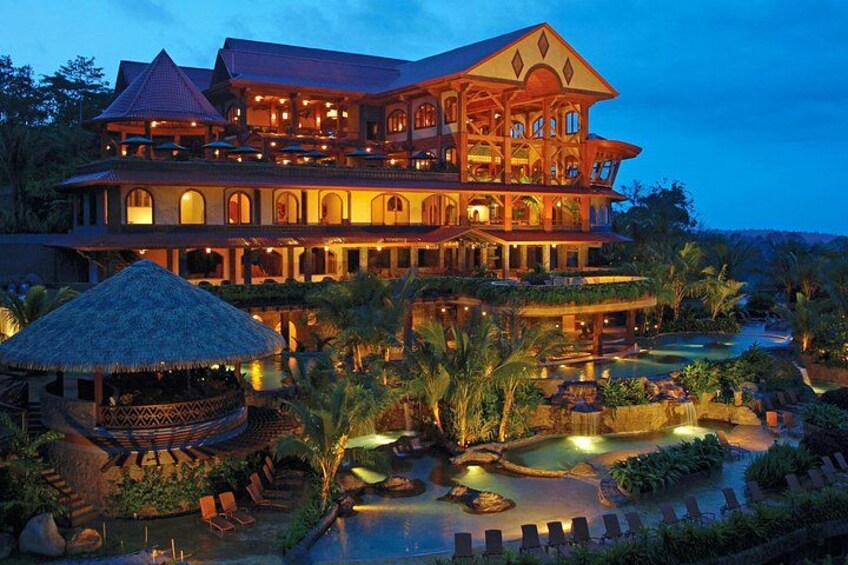 Ein großes, mehrstöckiges Resort mit Pool, Palmen und einem Gebäude mit einem Reetdach. 1