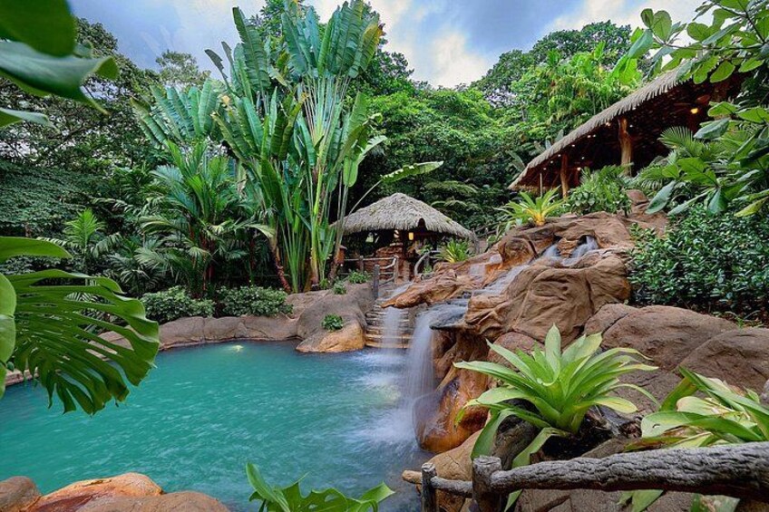 A tropical garden with a waterfall, a pool, and a thatched-roof hut. 5