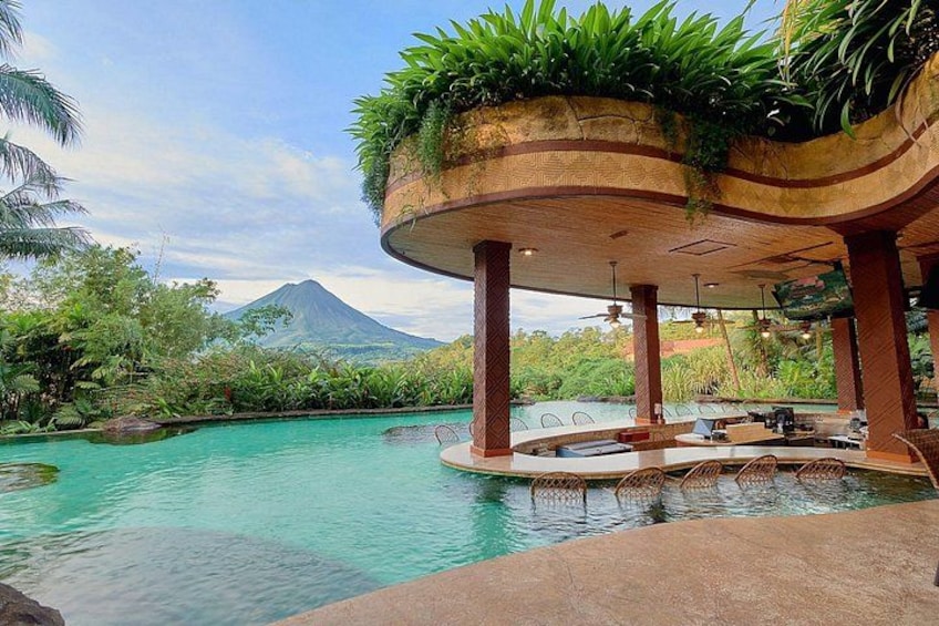 A pool with a tropical setting, a covered seating area, and a mountain in the background. 3
