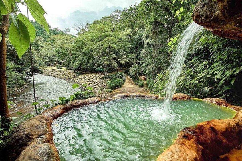 Ein natürlicher Thermalquell, umgeben von üppigem Grün und einem Wasserfall. 3