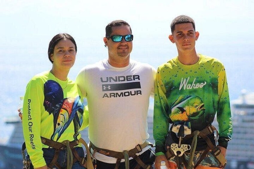 Tre persone con imbracature di sicurezza in piedi su una piattaforma, con uno skyline urbano sullo sfondo. 2