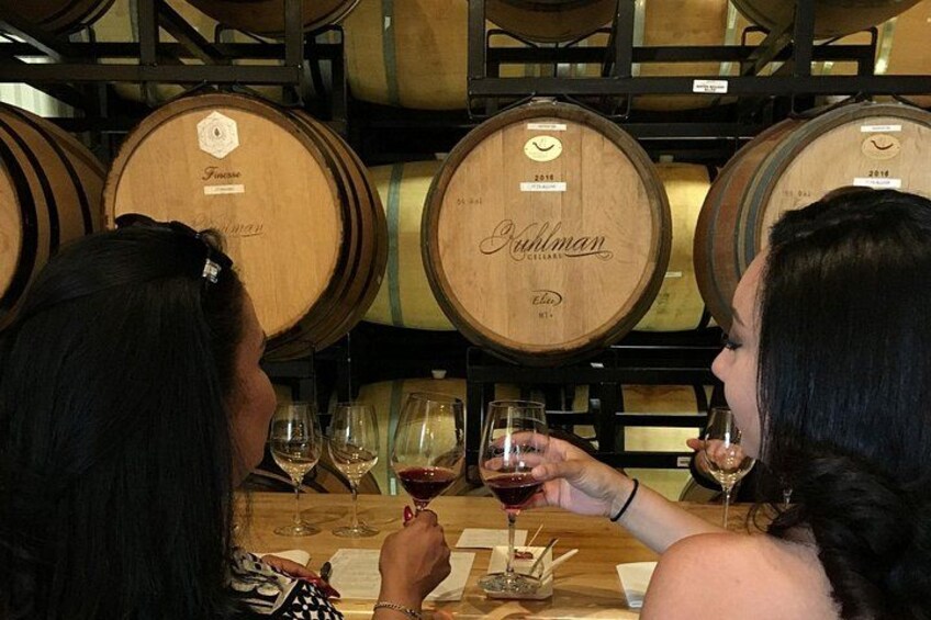 Zwei Personen verkosten Wein in einer Weinkellerei mit Holzfässern im Hintergrund. 1
